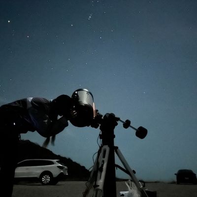 A dark nightime sky with a person in shadow viewing a telescope.